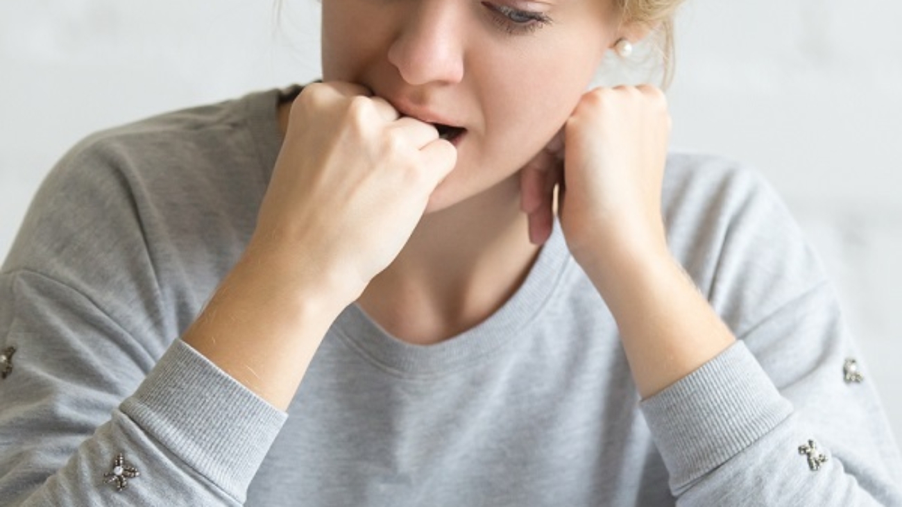 Portrait of a frustrated student girl sitting at the desk biting her fist. Education concept photo, lifestyle