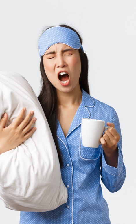 Morning lifestyle, breakfast and people concept. Girl with insomnia in sleeping mask and pajamas, hugging pillow, drinking coffee and yawning, trying wake-up, white background.