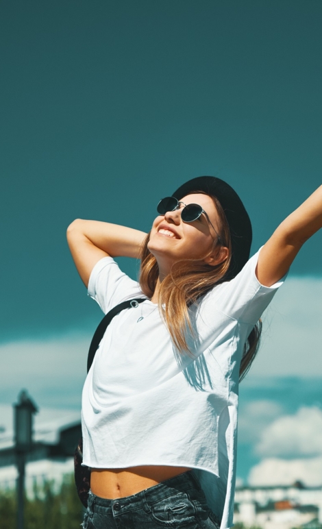 Freedom young woman carefree and happy with open arms on blue sky with hypnotizing sky in background. Caucasian girl in white shirt and jeans, feeling happiness enjoying her travel vacation