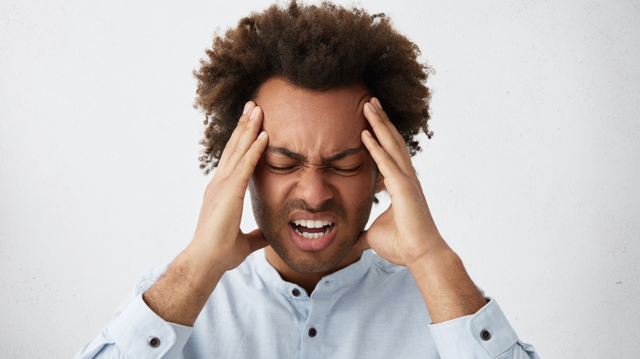 Stressed mixed race man with head of curly hair frowning his face holding hands on head having depression not knowing what to do suffering from headache having some serious problems in his life