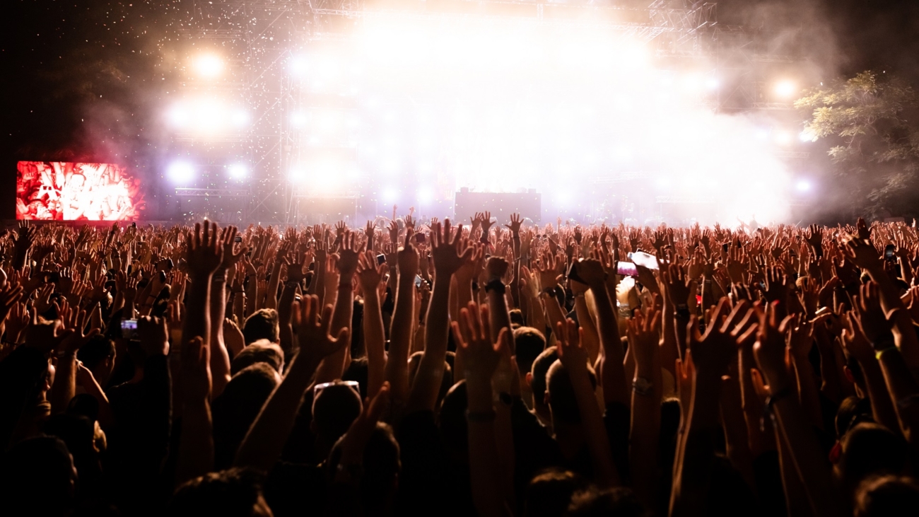 Rear view of excited people with arms raised having fun while watching confetti fireworks in front of the stage at music festival. Copy space.